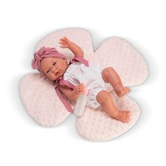Maria doll in a white romper, pink headband, with a floral pillow backdrop, holding a baby bottle.