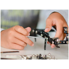 Child assembling metal construction set with a screwdriver, focusing on black perforated metal pieces connected with silver screws.