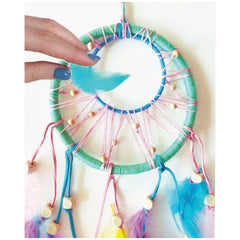 Hand holding a blue feather near a colorful dream catcher with wooden beads and vibrant threads.