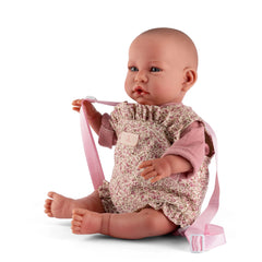 Realistic baby doll in a floral romper with pink sleeves and straps, sitting upright.