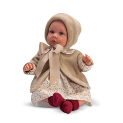 Asi Dolls 46 cm Leo in a cream outfit with a bow, floral dress, and red socks, sitting with hands up.
