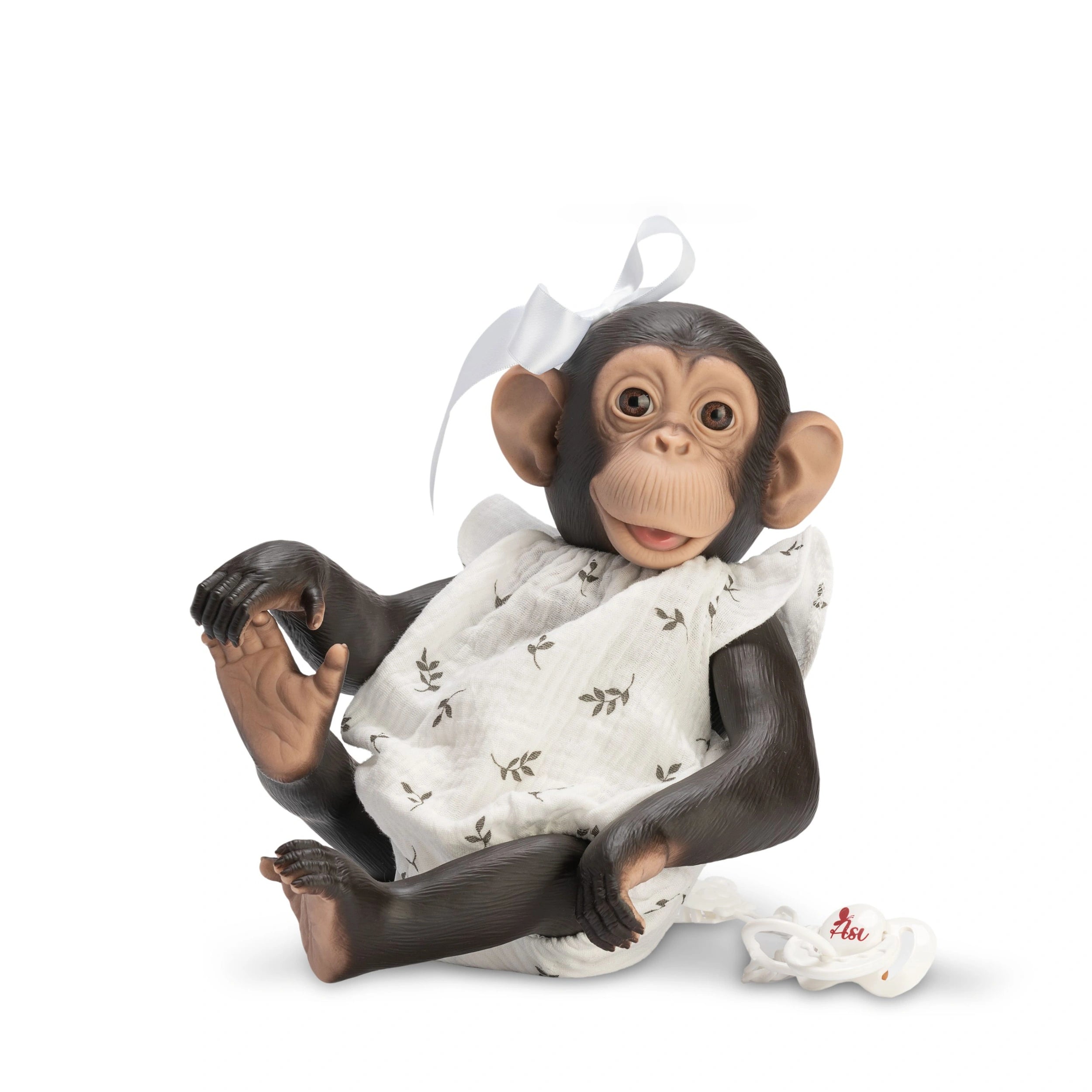 Lola chimpanzee doll in a floral onesie and white bow, sitting with a pacifier nearby.