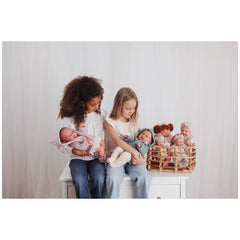 Two children holding Asi Dolls, with additional dolls displayed in a wicker basket, set against a light background.