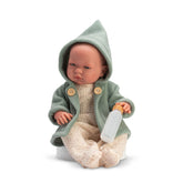 Baby doll Pablo from the Iris Collection wearing a green hooded coat, holding a bottle, and seated on a soft cushion.