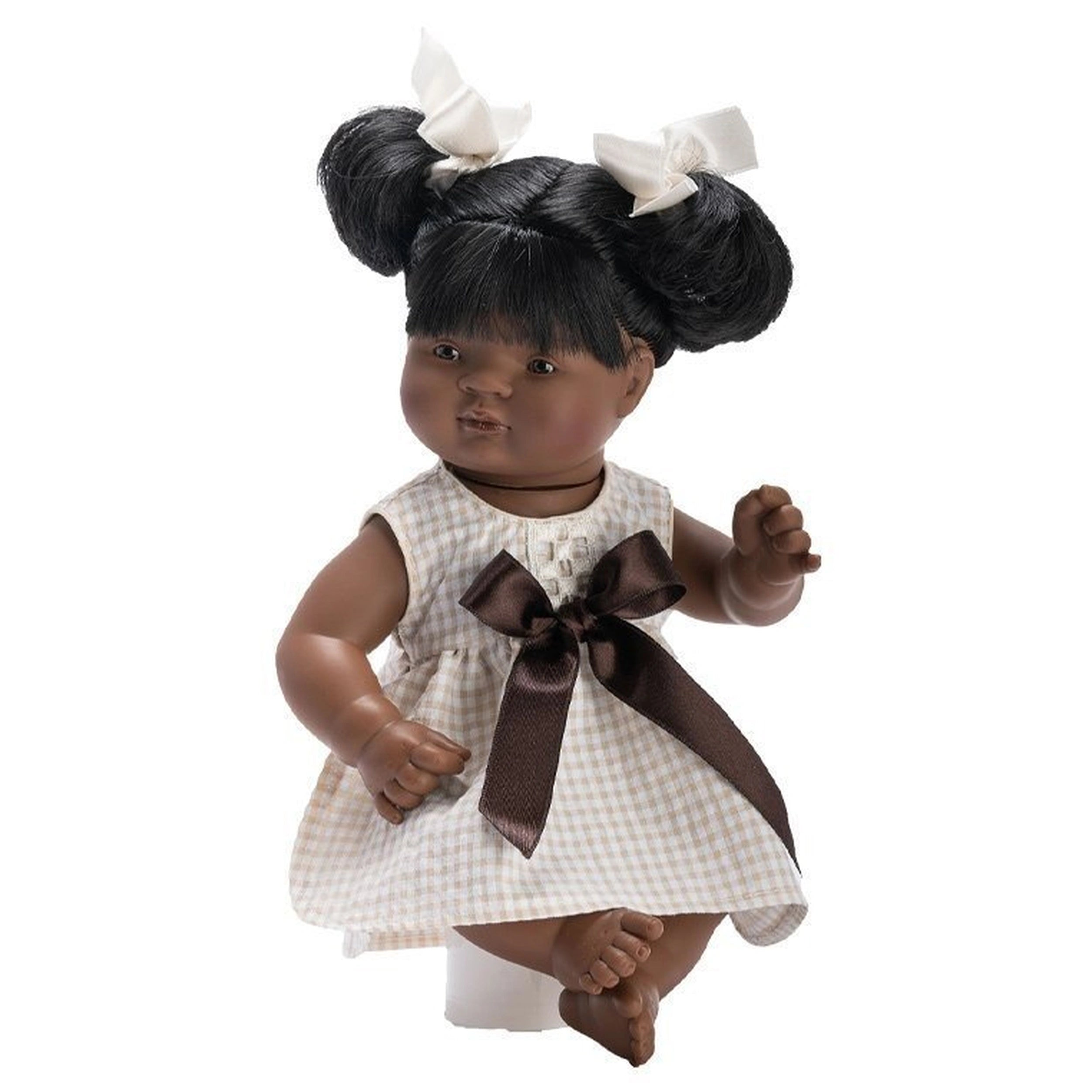 Samy 36 cm baby doll wearing a checkered dress with a brown bow, dual hair buns with white bows from the Sabana collection.