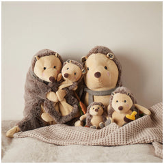 A cozy arrangement of four adorable hedgehog stuffed animals, featuring soft chocolate and oatmeal colors, snuggled together on a textured blanket.