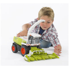 Child playing with Bruder Claas Jaguar 900 Field Chopper toy, featuring a detailed green and white design with rotating blades.