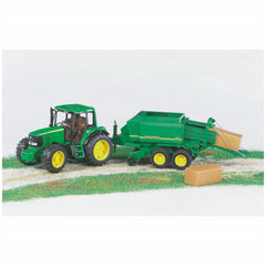 John Deere green toy tractor with yellow wheels and balepress on a field, producing a hay bale.