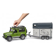 Hand playing with green Bruder Land Rover Defender and gray horse trailer toy, showcasing detailed design.
