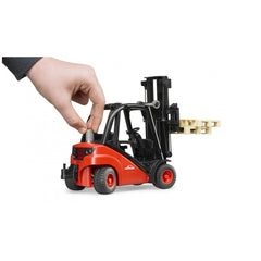 Red Bruder Linde Forklift toy with pallets, manipulated by a hand; realistic design, black and red color scheme.