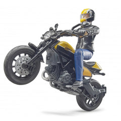 Rider in black gear performs a wheelie on a yellow and black 1:16 scale Bruder Scrambler Ducati toy motorcycle.