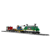 A LEGO® City Cargo Train with a green motorized engine, blue cargo car, and red trailer, positioned on black tracks.