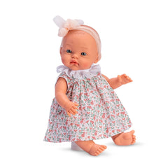 Alex doll in a floral salmon dress with lace collar and matching bow, bald head, sitting with arms open and light-colored eyes.