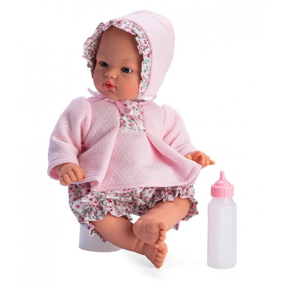 Koke doll in pink floral outfit with matching bonnet, sitting beside a pink baby bottle.