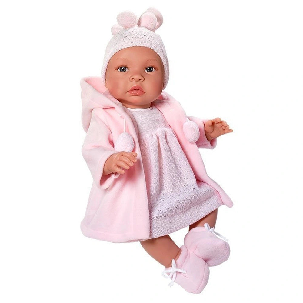 Doll wearing a pink knitted dress, duffle coat, and pom-pom hat, lying down with flexible vinyl limbs.