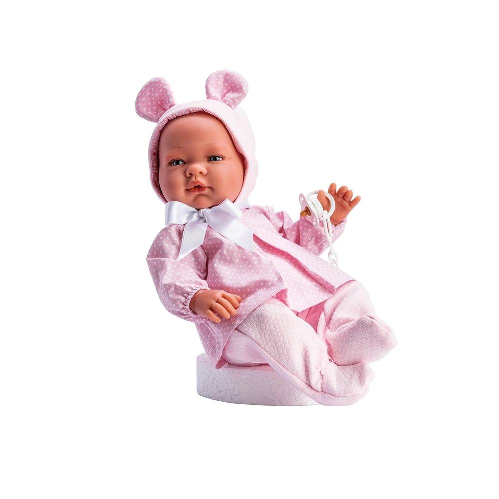 ASI Doll María in pink dress with hearts, wearing hat with ears, sitting on white surface, holding pacifier chain.
