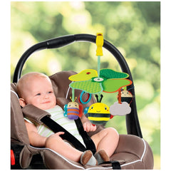 Baby Clementoni travel mobile activity toy hangs above a smiling child in a striped shirt seated in a brown car seat.