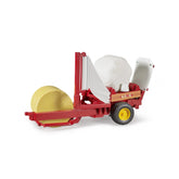 Red Bruder bale wrapper toy with yellow wheels and two round bales, showcasing realistic farm machinery for children.