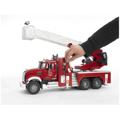 Child's hand operating Bruder Mack Granite fire engine toy with extendable ladder and water pump.