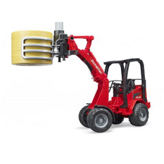 Red Bruder Schäffer Compact Loader 2630 with bale gripper holding a yellow bale, showcasing detailed farm vehicle features.