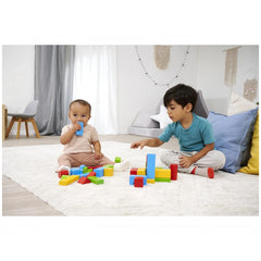 Eichhorn colored wooden blocks are scattered on a white carpet as two children play, one holding a blue block and the other a
