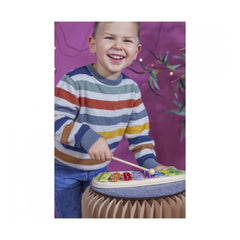 Eichhorn xylophone held by a smiling child in a colorful striped shirt against a vibrant purple background.