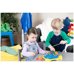 Goliath Let's Go Fishing game played by two children in denim overalls at a gray table, surrounded by colorful toys and decor