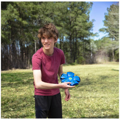 Young man in a red t-shirt holds a blue Wahu Phlat Ball frisbee with green and yellow circles in a green grassy setting.