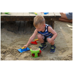 Gowi beach bucket in green and red, alongside blue and yellow shovels, as a child plays in the sand.