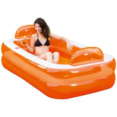 Woman in a black bikini relaxes on an orange and white pool float, holding a drink in a transparent cup.
