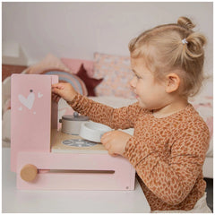 Blonde child in leopard print top playing with pink foldable cooker toy featuring various colorful labels and knobs.