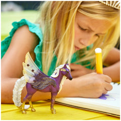 Schleich - Bayala - Star Pegasus Mare figurine is held by a girl at a bright yellow table while she writes in a notebook.