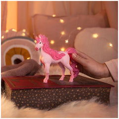 Cassiopeia Unicorn Mare toy in pink with a white face is held by a hand on a red star-patterned surface.