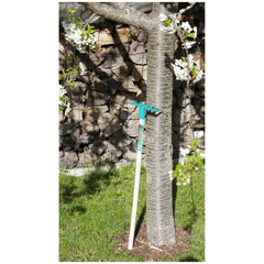Theo Klein Bosch Garden rake with a blue and white handle resting on green grass near a tree with white flowers.