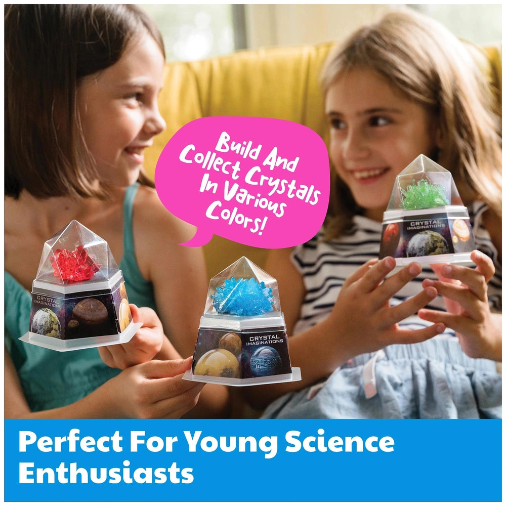 4M Crystal Growing Red Edition toy held by two smiling girls with colorful designs, clear casing, and yellow couch backdrop.