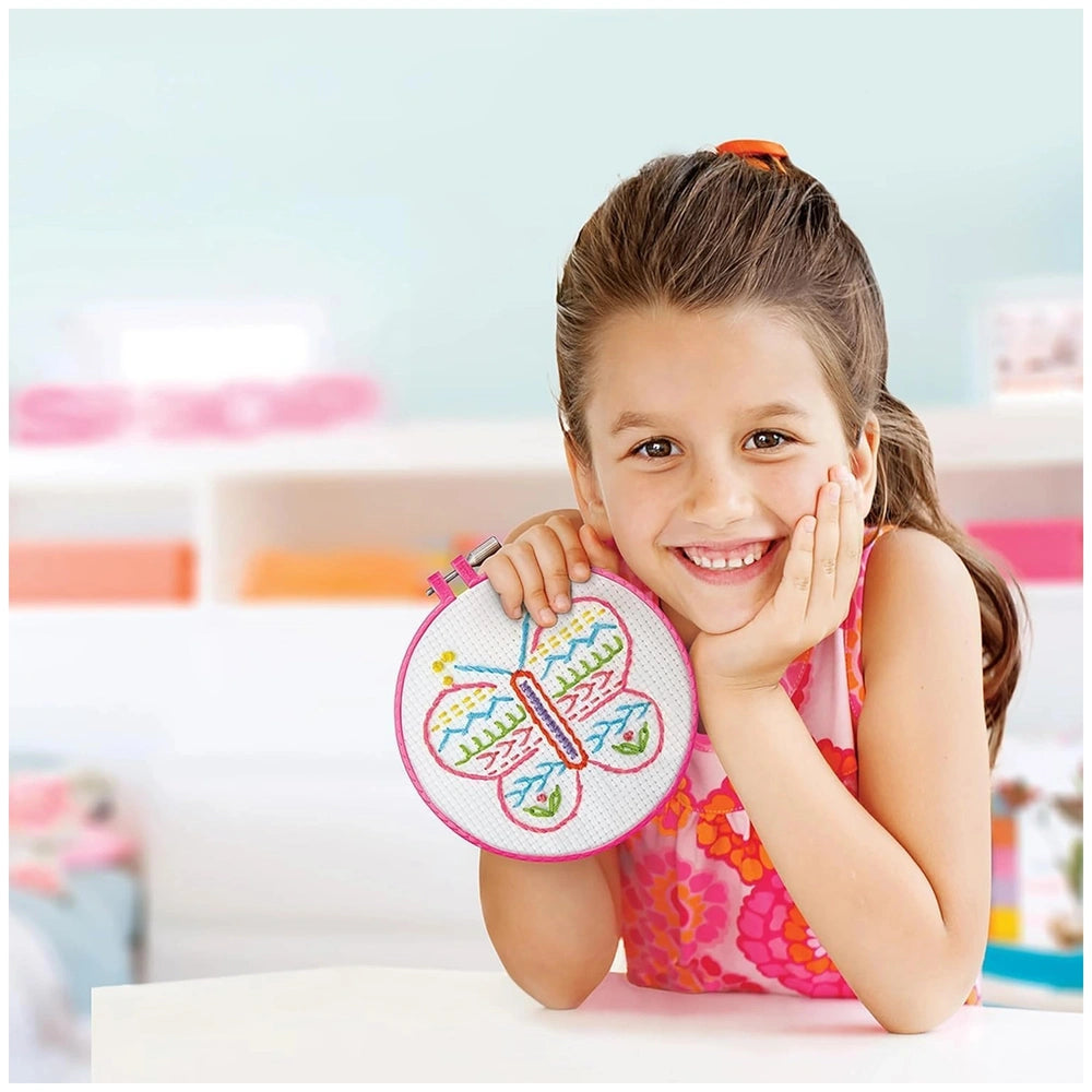 Girl in a pink floral dress embroiders pink and green stitches on a white table.