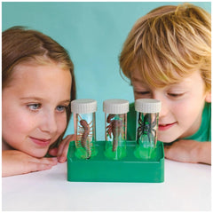 KidzLabs Glow Critter Lab toy playset displayed on a white tabletop with two children in green tops engaging with it.