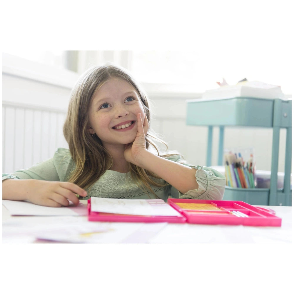 a young girl in a light green top holds a pink folder at a white table with various papers, in front of a blue desk.