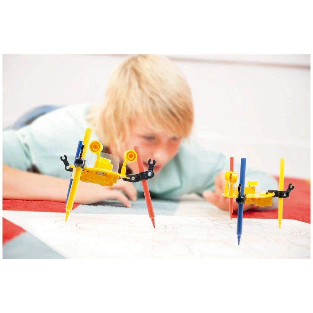 KidzRobotix Doodling Robot with colorful wheels, held by a person in a light blue shirt on a red surface.
