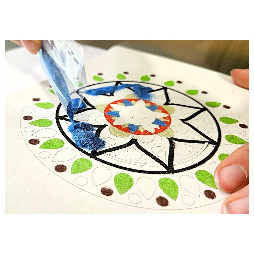 Blue glitter being applied from a clear plastic bag onto a circular design on a white surface.