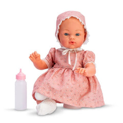 Asi Dolls Koke baby doll in a pink floral dress and bonnet, seated with a pink baby bottle beside it.