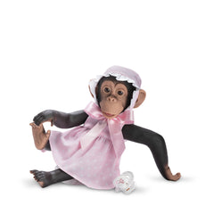 Lifelike Lola the Chimpanzee doll in a pink dress with white stars, wearing a bonnet, sitting with a pacifier nearby.