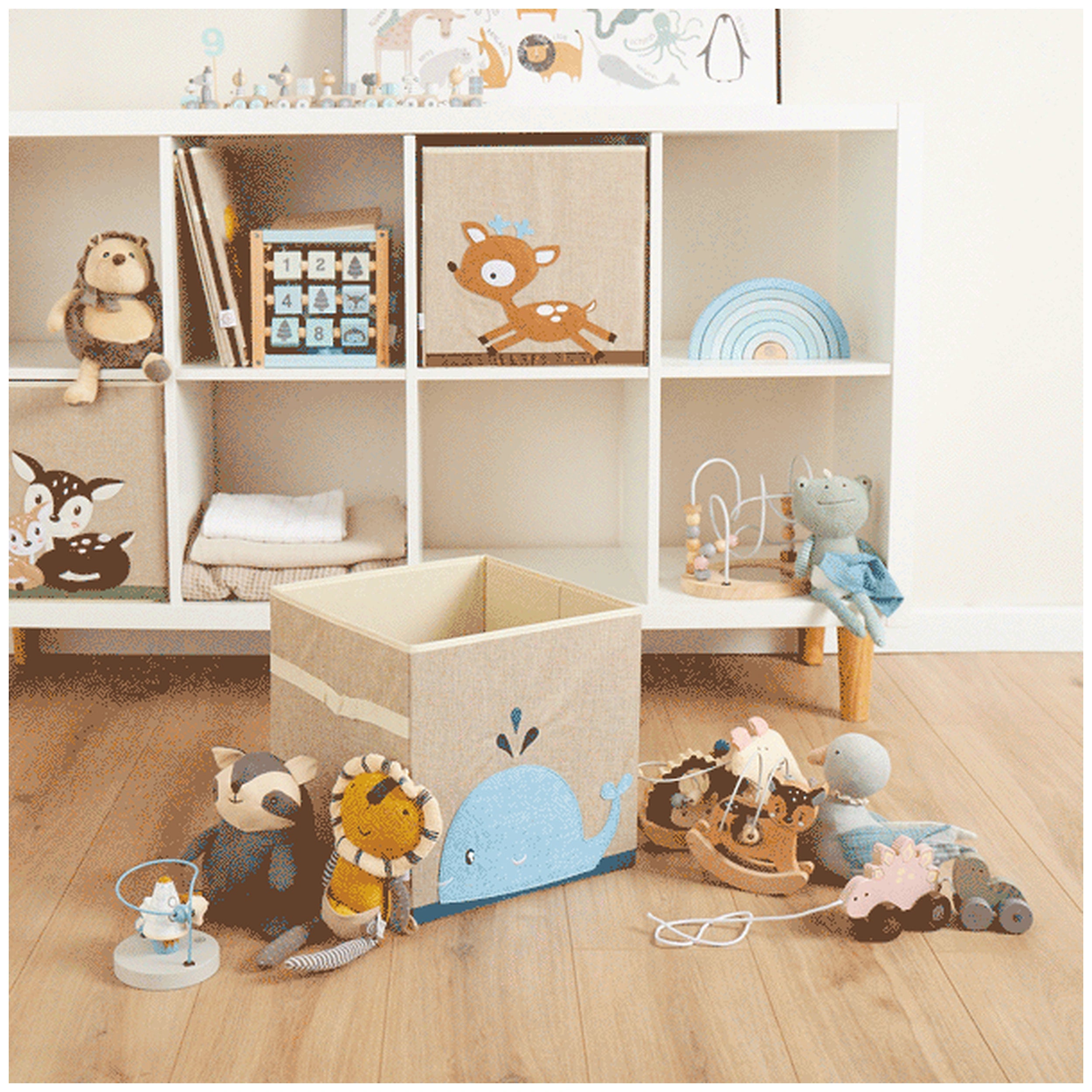 Whale storage box in sand and sky blue, surrounded by soft toys and wooden games on light wooden floor, enhancing a children's room.
