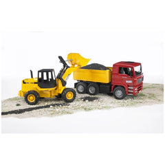 Yellow articulated road loader unloading into red construction truck on sandy terrain.