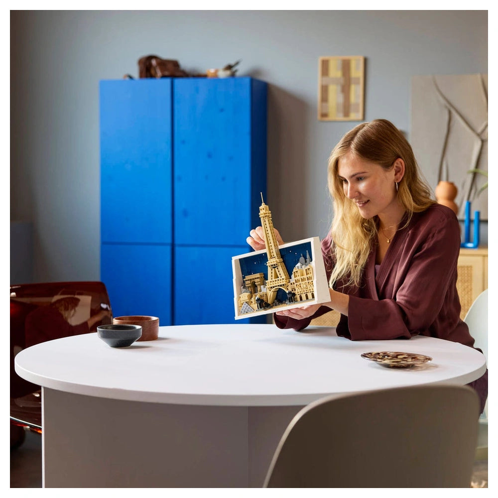 LEGO Architecture Paris set displayed with a woman reading a book featuring the Eiffel Tower in a modern, stylish room.