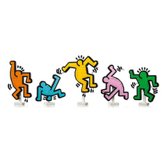 Five colorful LEGO figures inspired by Keith Haring's art, featuring vibrant orange, blue, yellow, pink, and green dancing motifs with playful poses.