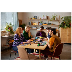 Five diverse friends sitting around a wooden table, joyfully assembling the LEGO® Art Keith Haring Dancing Figures set, surrounded by colorful building pieces and a cozy, well-lit room.