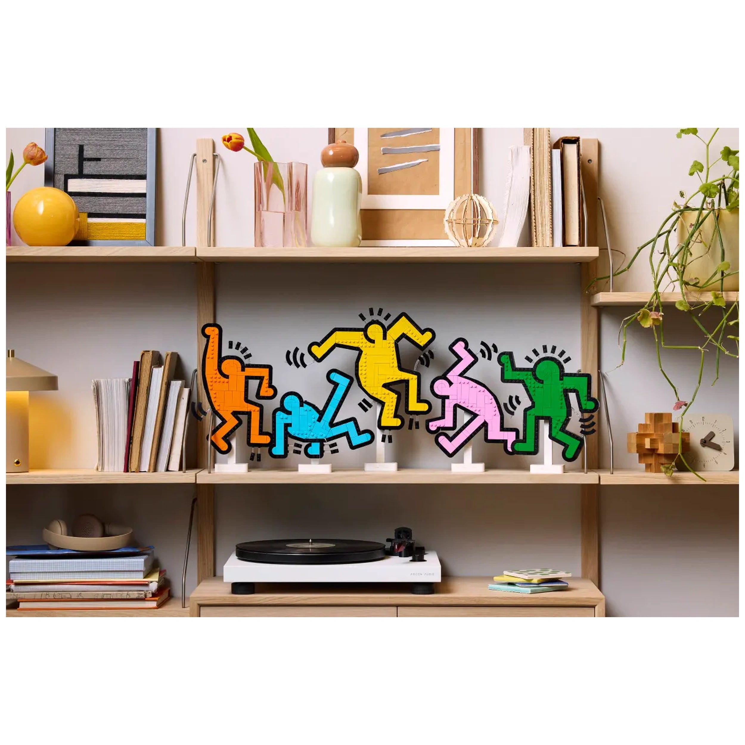 Colorful dancing figures inspired by Keith Haring, displayed on a wooden shelf among books and decor.