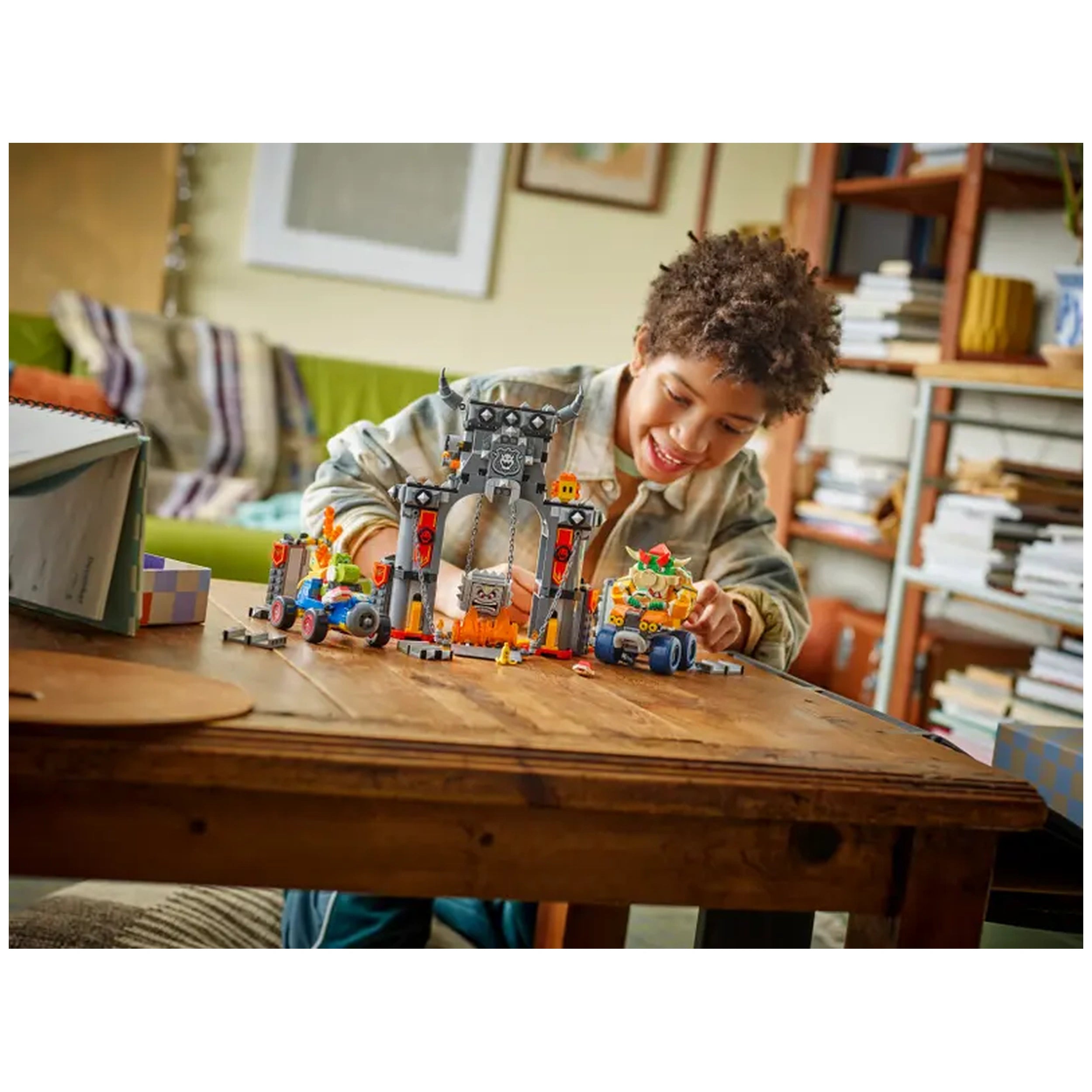 A joyful child interacts with the LEGO Bowser's Castle playset, featuring detailed characters and a dynamic racetrack, on a wooden table.