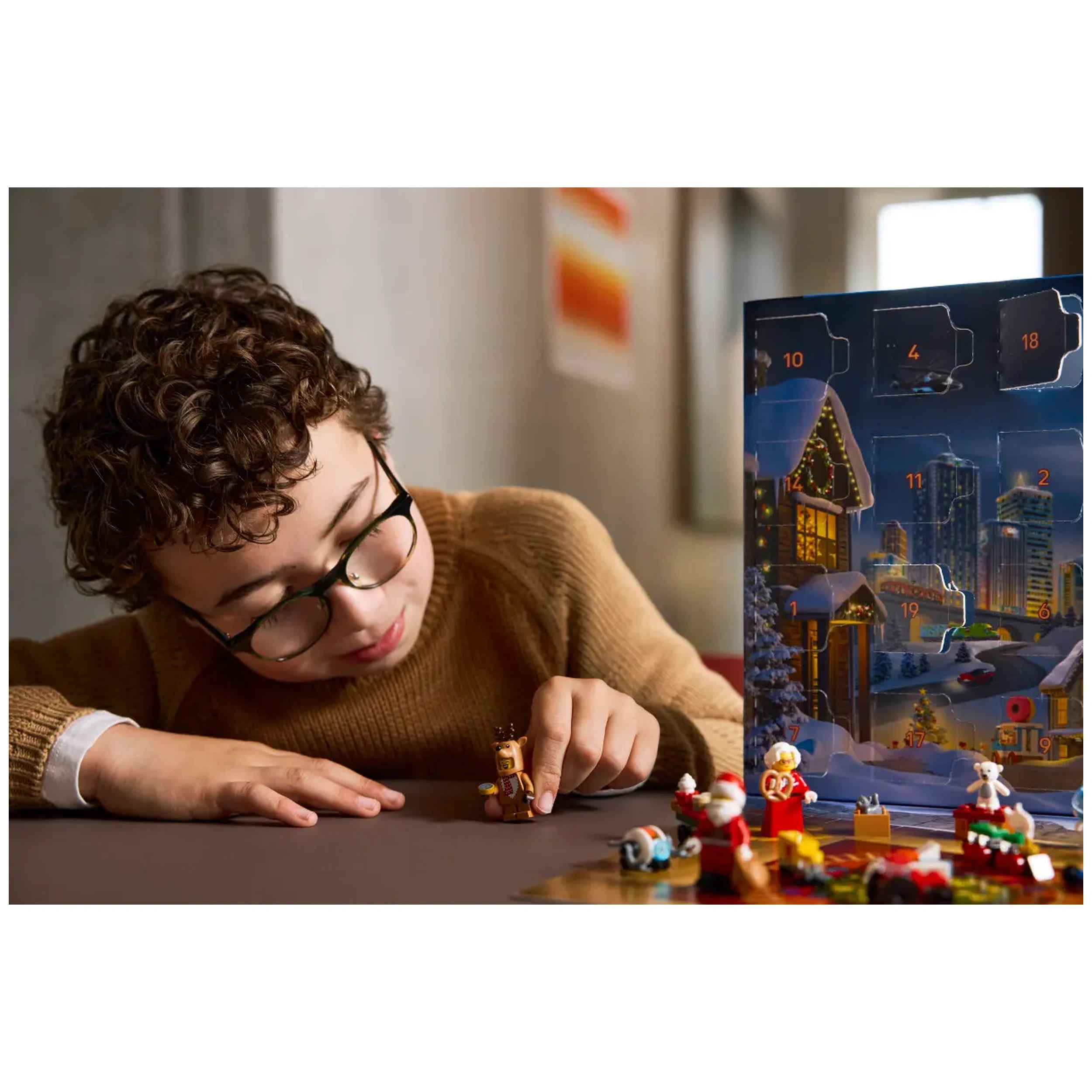 A child with curly hair and glasses focuses intently on building a LEGO mini figure, surrounded by colorful holiday-themed accessories from the LEGO City Advent Calendar 2025. In the background, a festive advent calendar displays numbered doors and a snowy village scene, adding to the enchanting atmosphere of imaginative play.
